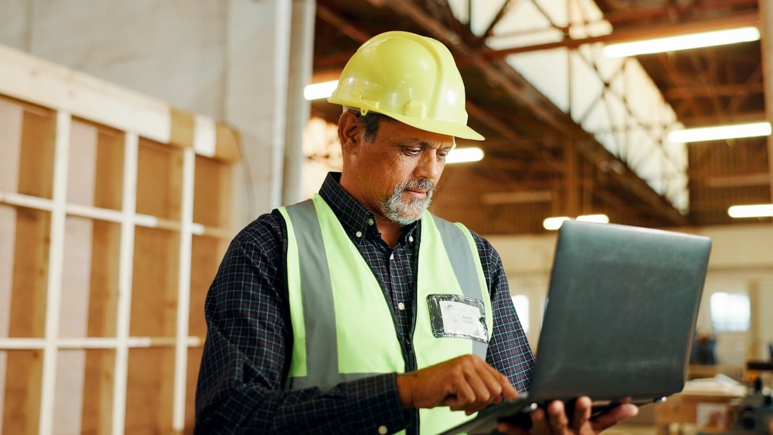 Carpenter using a laptop in a workshop to plan furniture restoration, showing digital project management in a construction and renovation setting.