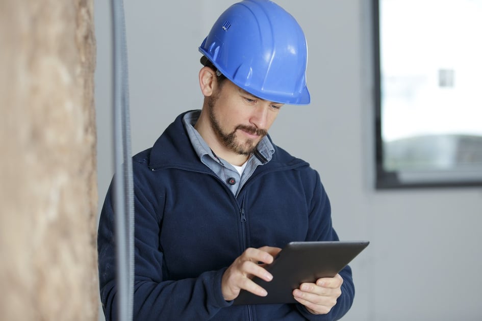 Workman using a tablet inside a renovation property to manage project details and track restoration progress.